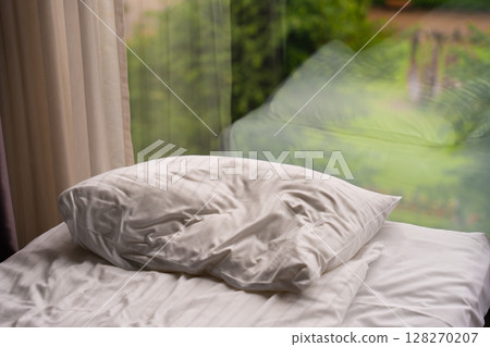 White pillow on unmade bed near window with garden reflection White pillow on unmade bed near window with garden reflection 128270207