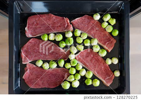 Raw pork steaks and Brussels sprouts on oven tray ready for roasting in the kitchen. Selective focus Raw pork steaks and Brussels sprouts on oven tray ready for roasting in the kitchen. Selective focus 128270225