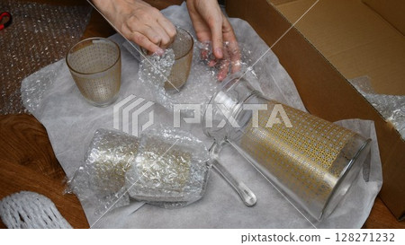 Hands pack up and wrap glassware into plastic bubble wrapping Hands pack up and wrap glassware into plastic bubble wrapping 128271232