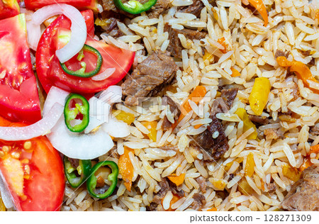 A rice dish with meat, garnished with a salad of chopped tomatoes, onions and hot green chili peppers. The photo is suitable for both the restaurant business and any food related design 128271309