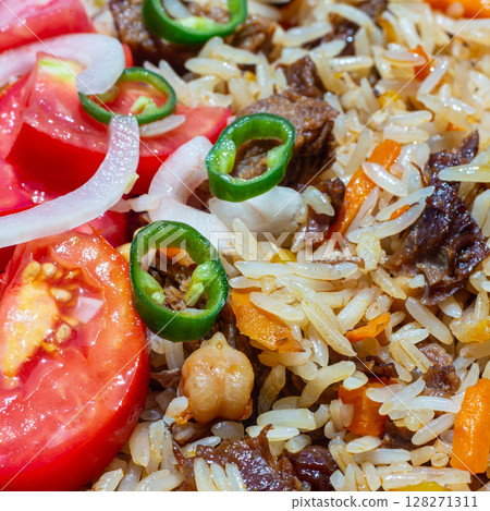 A rice dish with meat, garnished with a salad of chopped tomatoes, onions and hot green chili peppers. The photo is suitable for both the restaurant business and any food related design 128271311