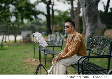 Man rests with trumpet beside music stand, enjoying a quiet moment in nature 128271638
