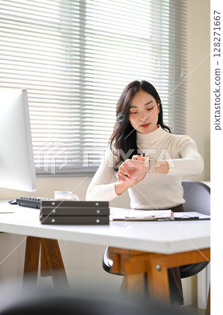 Businesswoman checking time on smartwatch, managing schedule in a bright office 128271667