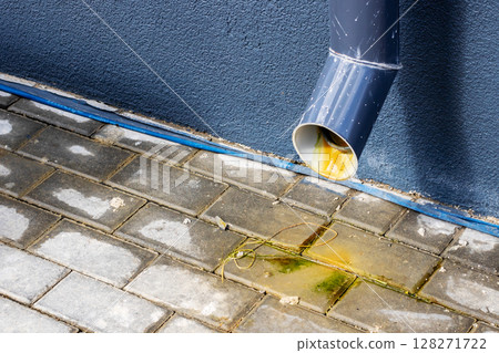 There is a noticeable leak coming from a drain pipe onto the brick sidewalk 128271722