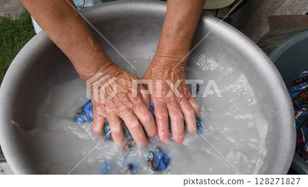 Aged wrinkled hands of 80s senior woman crumpling textile while handwash laundry 128271827