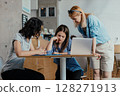 Three female colleagues reviewing meeting notes and feedback in bright office cafeteria 128271913