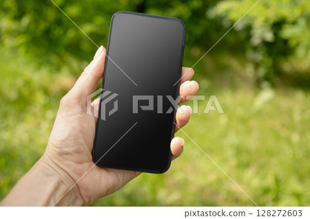 Close up of womans hands holding smartphone in outdoor green setting. Check apps, focused on device, chatting, performance data. Voice assistant. Fitness progress on app. Space for design on screen. 128272603