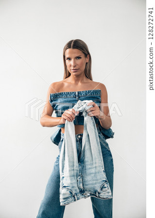Model showcases denim outfit in modern studio setting while holding a jacket 128272741