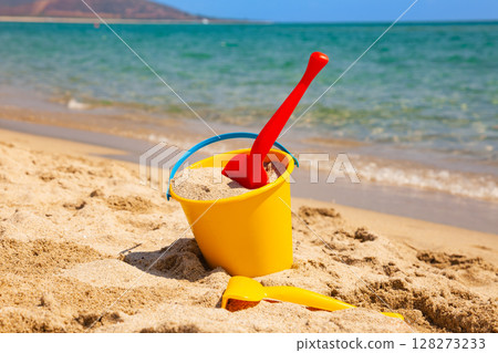 Yellow bucket with red plastic shovel filled with sand on sunny beach Yellow bucket with red plastic shovel filled with sand on sunny beach 128273233