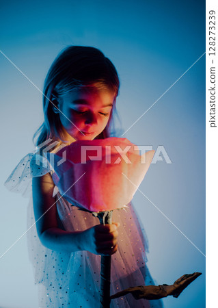 Young girl admires glowing rose in soft blue light during enchanting indoor moment 128273239