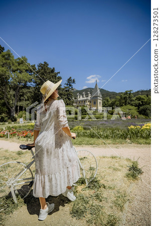 A woman in a white dress is standing next to a bicycle 128273501