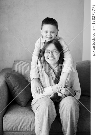 Little boy hugging his older sister. Happy siblings smiling to camera. Adorable kids having fun together at home. Black and white image. 128273772