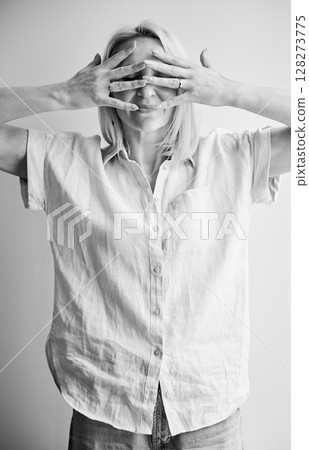 Pretty woman hiding face in her hands. Beautiful female covering face by fingers. Young woman in casual clothes posing on light background. Black and white image. 128273775