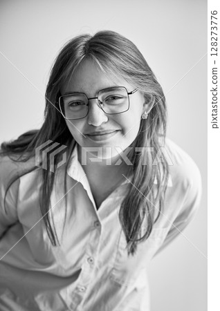 Portrait of beautiful girl smiling to camera. Cute girl in cream shirt and square glasses posing on white background. Black and white image. 128273776
