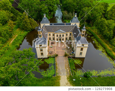 Aerial view of a historic castle surrounded by a forest, with vast green fields, winding waterways, and a river stretching across the flat Dutch countryside under a partly cloudy sky. 128273908