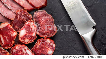 macro photo of raw dried sliced horse meat sausage and silver knife on black marble surfac 128274006