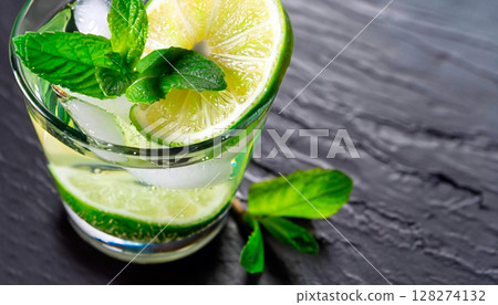 macro shot glass of mojito with sliced lime and mint on black stone surface 128274132