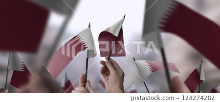 Qatar flags in their hands on a blurred urban background 128274282