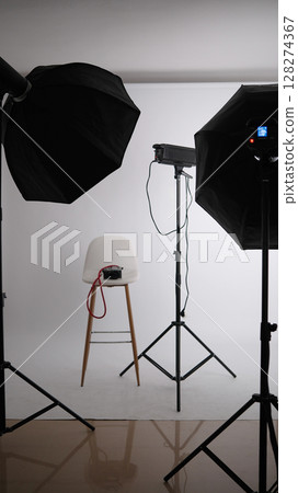 Empty stool surrounded by professional lighting equipment in photo studio Empty stool surrounded by professional lighting equipment in photo studio 128274367