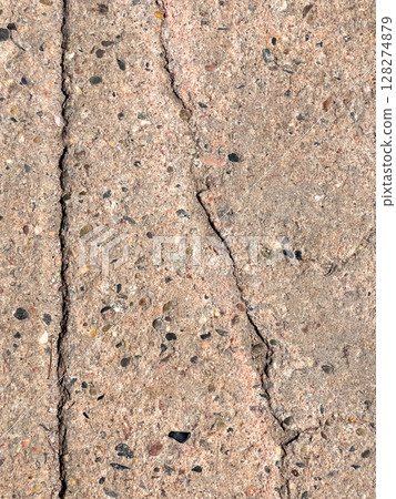 Detailed image of a cracked concrete pavement showing visible texture and embedded stones. The cracks form an organic pattern, adding visual interest. Suitable for illustrating aging surfaces 128274879