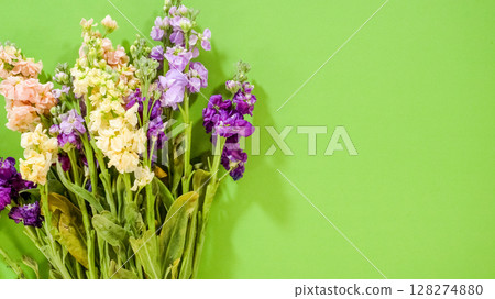 Mixed flower stems including soft pinks and purples are positioned on a green surface, ready for wrapping. The vibrant color contrast adds a cheerful tone. 128274880