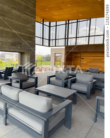 A spacious community lounge with modern patio furniture, floor-to-ceiling windows, and a large concrete fireplace. The room features a wood-paneled ceiling and open-air views of surrounding homes and A spacious community lounge with modern patio furniture, floor-to-ceiling windows, and a large concrete fireplace. The room features a wood-paneled ceiling and open-air views of surrounding homes and 128274899