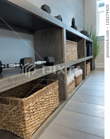A complete view down the side of a gym shelf lined with weights, towels, and baskets. Light streaming in from the window adds warmth. 128274920
