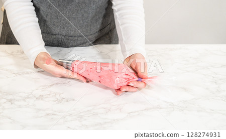 A piping bag filled with vibrant cranberry buttercream, ready to decorate the lemon spritz cookies. This rich and colorful buttercream adds the perfect tangy-sweet touch to the lemony cookies, making 128274931