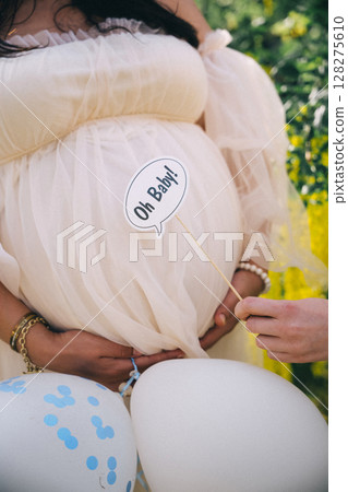 Celebration of motherhood with a pregnant woman holding balloons and a sign in a garden setting Celebration of motherhood with a pregnant woman holding balloons and a sign in a garden setting 128275610