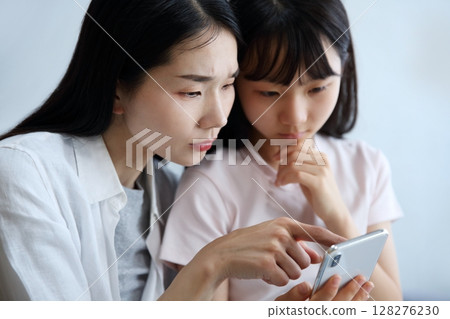 一位母親和女兒認真地看著智慧型手機的圖片 128276230