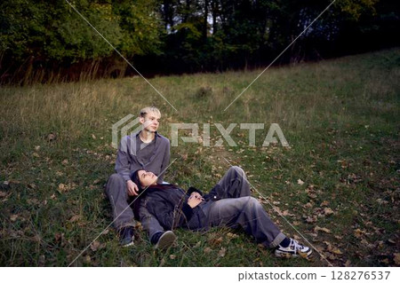 15-year-old teenage couple in love lies, sits on the grass in the park surrounded by fallen autumn leaves 128276537