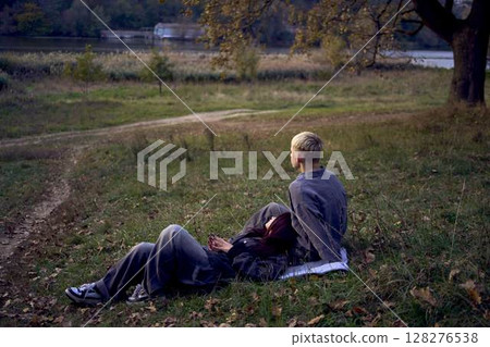 15-year-old teenage couple in love lies, sits on the grass in the park surrounded by fallen autumn leaves 128276538