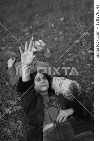 15-year-old teenage couple in love lies, sits on the grass in the park surrounded by fallen autumn leaves 128276543