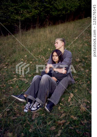 15-year-old teenage couple in love lies, sits on the grass in the park surrounded by fallen autumn leaves 128276545