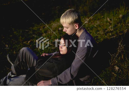15-year-old teenage couple in love lies, sits on the grass in the park surrounded by fallen autumn leaves 128276554