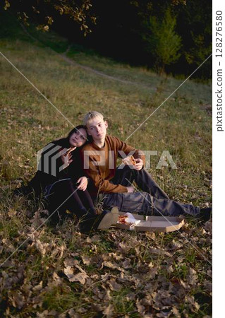 15-year-old teenage couple in love eating pizza on a picnic in an autumn park 15-year-old teenage couple in love eating pizza on a picnic in an autumn park 128276580