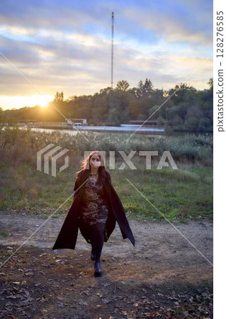a 15-year-old teenage girl in a black long coat at sunset by the river a 15-year-old teenage girl in a black long coat at sunset by the river 128276585