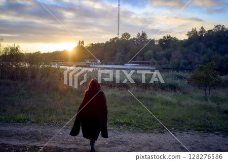 a 15-year-old teenage girl in a black long coat at sunset by the river a 15-year-old teenage girl in a black long coat at sunset by the river 128276586