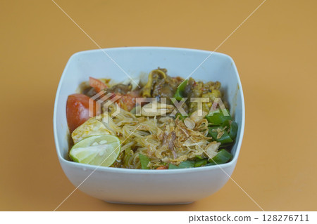 A flavorful Indonesian dish featuring vermicelli, vegetables, and meat, garnished with fried shallots and lime, served in a white bowl. A flavorful Indonesian dish featuring vermicelli, vegetables, and meat, garnished with fried shallots and lime, served in a white bowl. 128276711