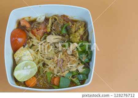 A flavorful Indonesian dish featuring vermicelli, vegetables, and meat, garnished with fried shallots and lime, served in a white bowl. A flavorful Indonesian dish featuring vermicelli, vegetables, and meat, garnished with fried shallots and lime, served in a white bowl. 128276712