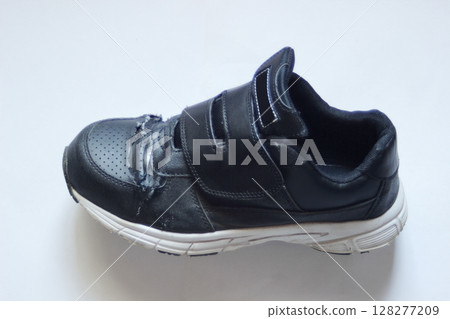 A pair of synthetic leather Velcro-fastened sneakers with a torn upper part placed diagonally sideways on a piece of white paper A pair of synthetic leather Velcro-fastened sneakers with a torn upper part placed diagonally sideways on a piece of white paper 128277209