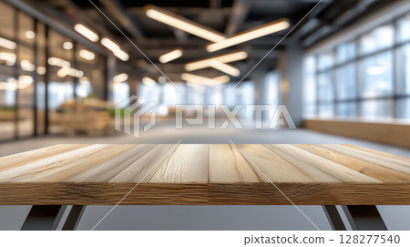 A clean wooden table surface in a modern office with blurred bright lights and glass walls in the background 128277540