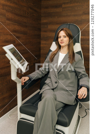 Vertical portrait of young businesswoman in suit sitting on ergonomic chair for pelvic floor muscle examination in modern clinic, looking at camera. Concept of advanced healthcare technology. Vertical portrait of young businesswoman in suit sitting on ergonomic chair for pelvic floor muscle examination in modern clinic, looking at camera. Concept of advanced healthcare technology. 128277846