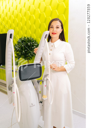 Vertical portrait of cosmetic professional doctor posing with new modern mesotherapy apparatus, holding handles, showcasing professional equipment for advanced skincare treatments, looking at camera. 128277859