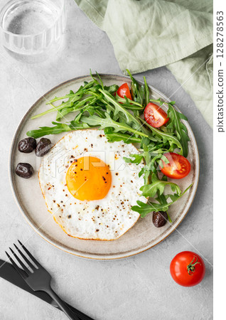 Fried eggs with arugula, ovives  and cherry tomatoes on a plate on a light background 128278563