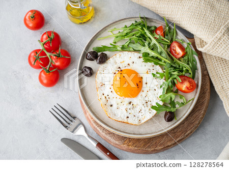 Fried eggs with arugula, ovives  and cherry tomatoes on a plate on a wooden board  128278564