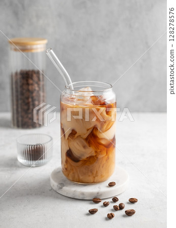 Ice latte coffee in a glass with milk on a marble board on a light background with coffee beans. Ice latte coffee in a glass with milk on a marble board on a light background with coffee beans. 128278576