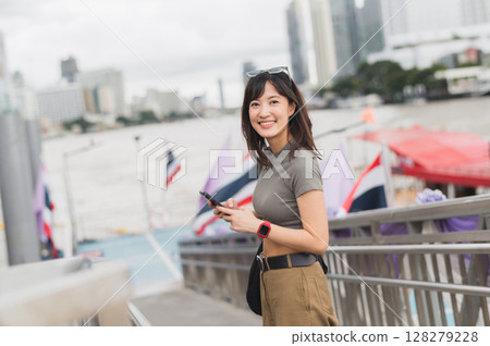 Young southeast asian woman teenager blogger using smartphone searching for travel guide. world explorer on local cultural experience near Chao Phraya river Bangkok. Asia tourism concept Young southeast asian woman teenager blogger using smartphone searching for travel guide. world explorer on local cultural experience near Chao Phraya river Bangkok. Asia tourism concept 128279228