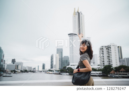 Happy solo young southeast asian woman teenager blogger explorer on world travel. Asia tourism concept for local cultural experience with smartphone by Chao Phraya River in Bangkok Thailand 128279247