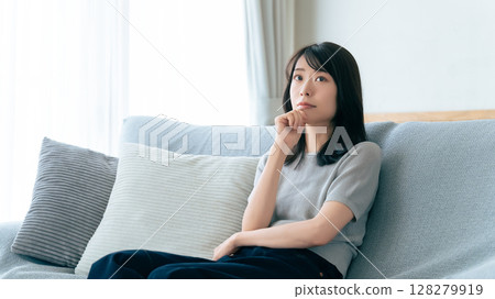 A woman sitting on a sofa and thinking 128279919